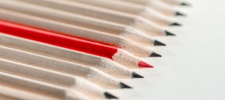 A single red pencil among a row of beige pencils.